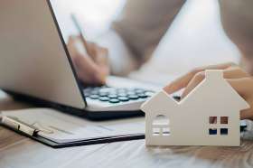 Foto: Person bearbeitet Akten, Modell eines Hauses im Vordergrund